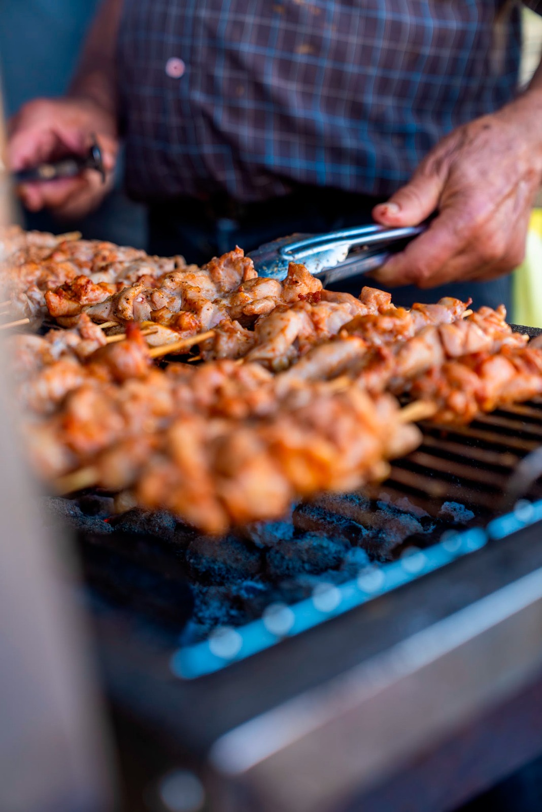 Chicken souvlakia turned with tongs over the charcoal
